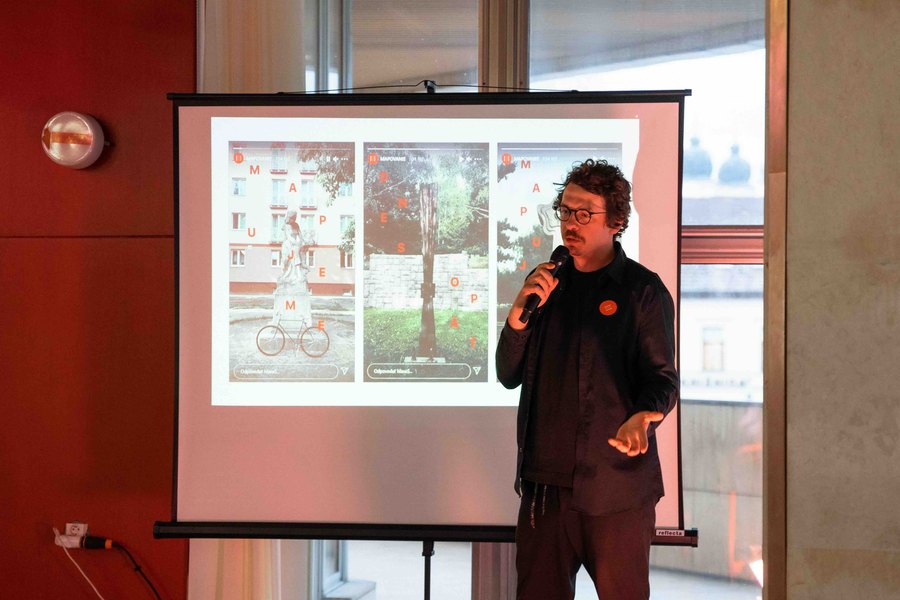 Prednášajúci s mikrofónom pred premietacím plátnom počas večerného programu
