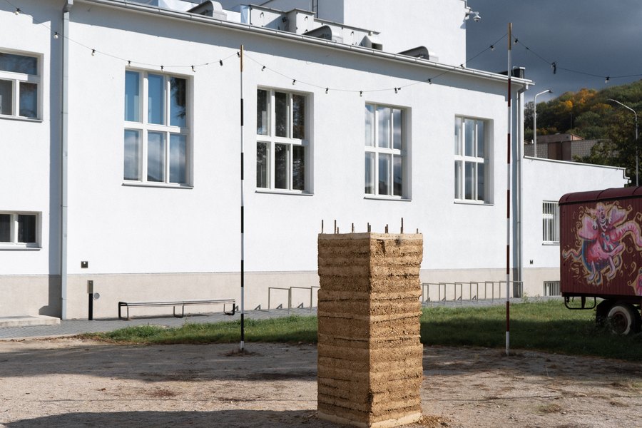 Monolit z dusanej hliny s viditeľnými vrstvami na štrkovej ploche pred bielou budovou