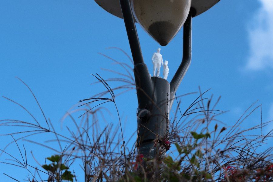 Dve biele figúrky na ramene pouličnej lampy proti oblohe